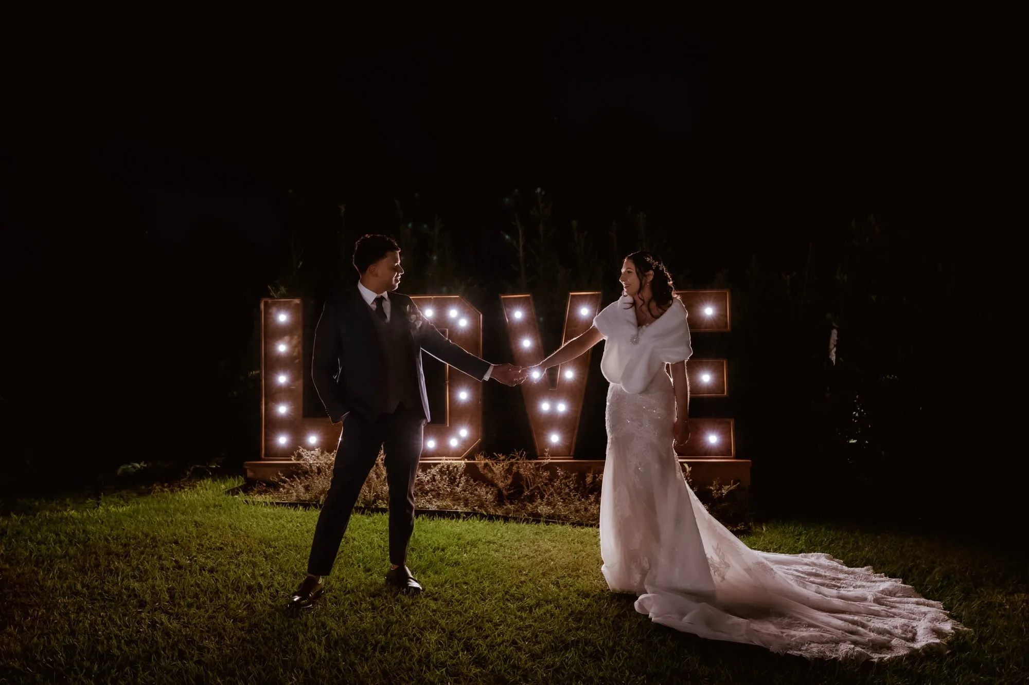 Couple holding hands in front of a love sing at night